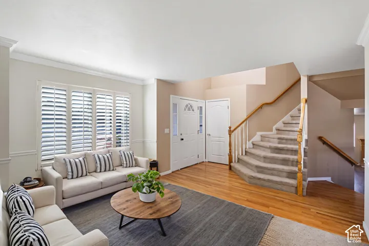 Interior space featuring wood-finish flooring, plantation shutters, crown molding, chair rail trim, and a staircase with a wooden handrail