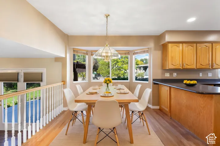 Dining area featuring wood-finish flooring, a bay window, light wood cabinetry with dark countertops, and a pendant light fixture