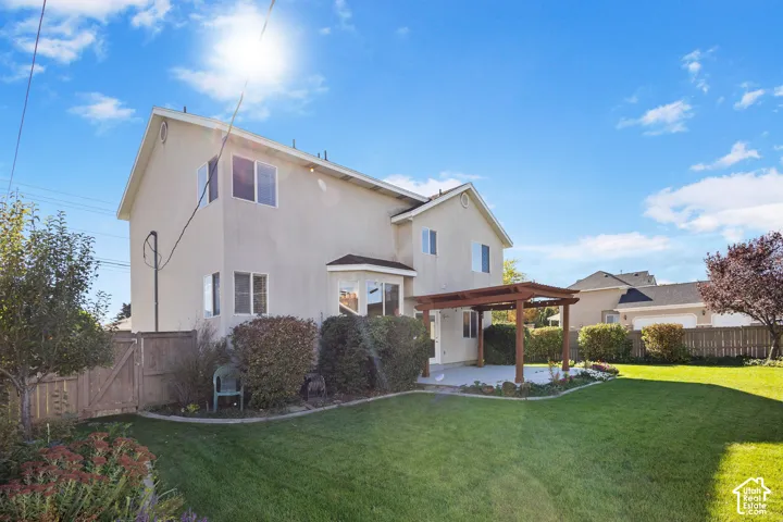 Two-story exterior featuring a stucco facade, backyard lawn, wood-framed pergola, and privacy fencing