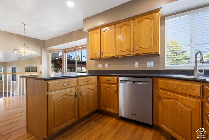 Kitchen featuring wood cabinetry, dark solid-surface countertops, stainless steel dishwasher, bay window, and wood-finish flooring