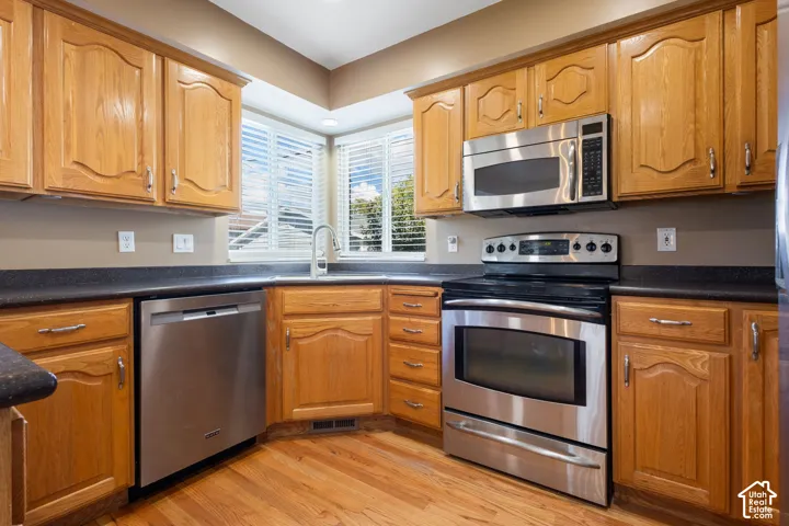 Kitchen featuring wood cabinetry, stainless steel appliances, dark countertops, and wood-finish flooring