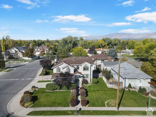 Two-story residence featuring light-toned exterior cladding, a multi-gabled roof, arched window detailing, and a manicured corner lot with mature landscaping