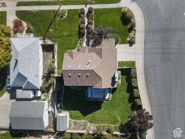 Aerial view of property featuring a concrete driveway, multi-gabled asphalt shingle roof, expansive lawn, backyard patio cover, and perimeter landscaping