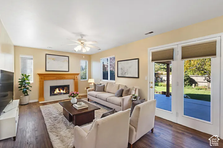 Living area featuring wood-finish flooring, a fireplace with a wood mantel, a ceiling fan, and double glass doors opening to a concrete patio