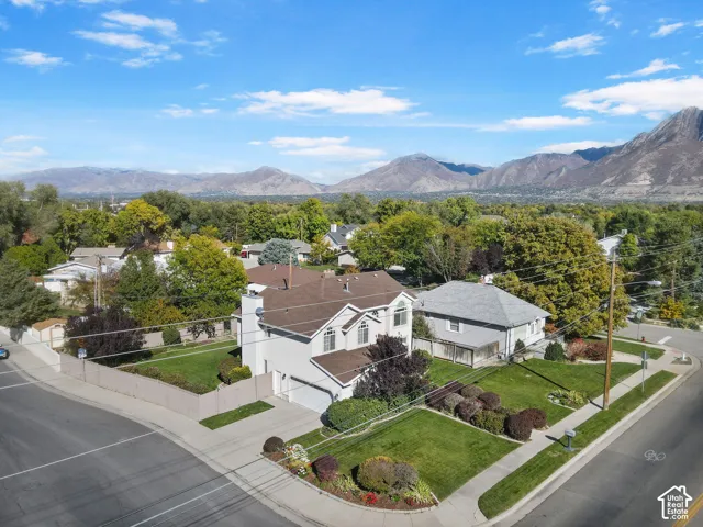 Two-story residence featuring a shingled roof, exterior chimney, attached garage, fenced yard, and mountain backdrop