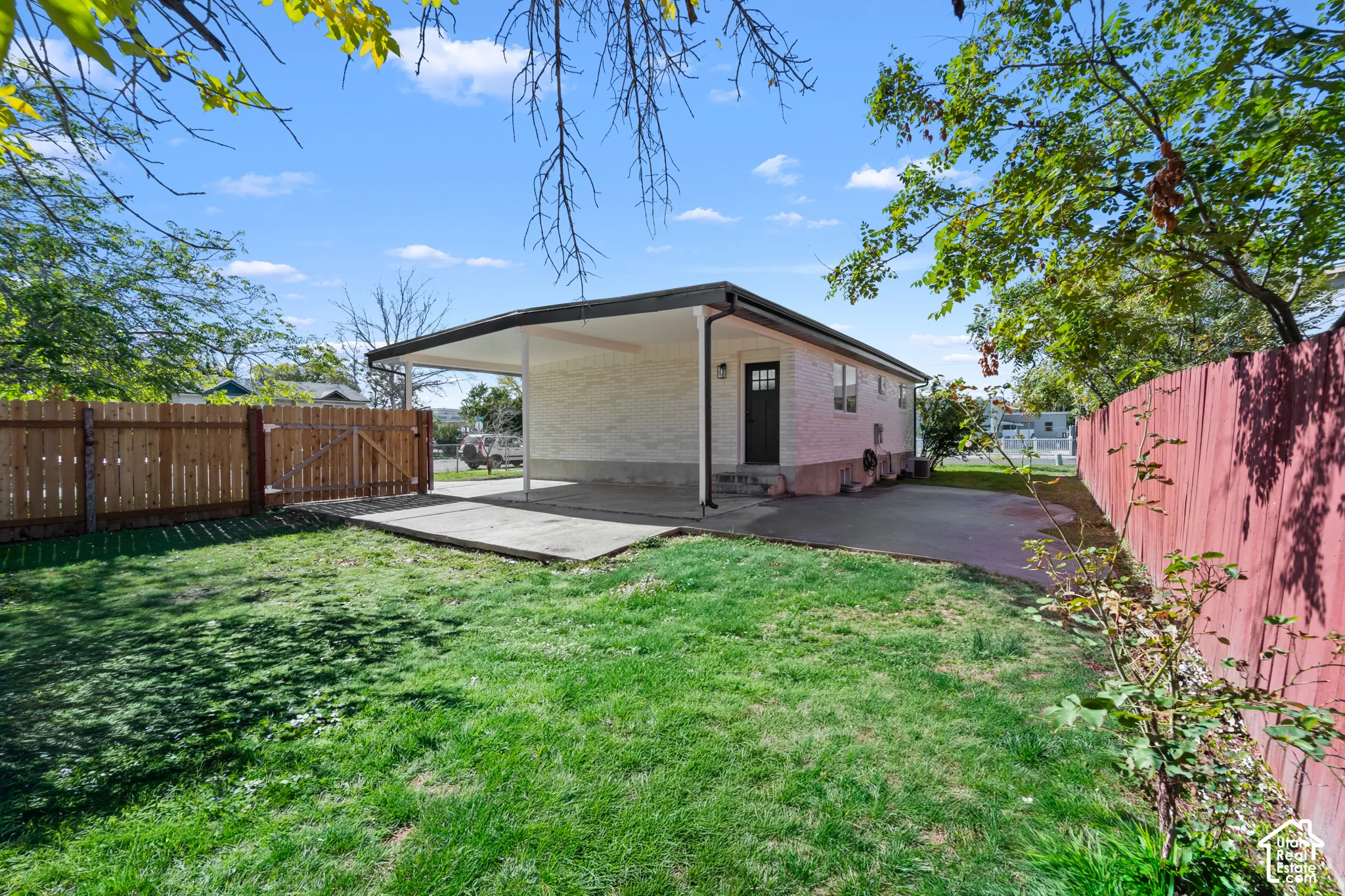 Exterior featuring a painted brick facade, covered carport, concrete patio, and fenced backyard with wood privacy screening