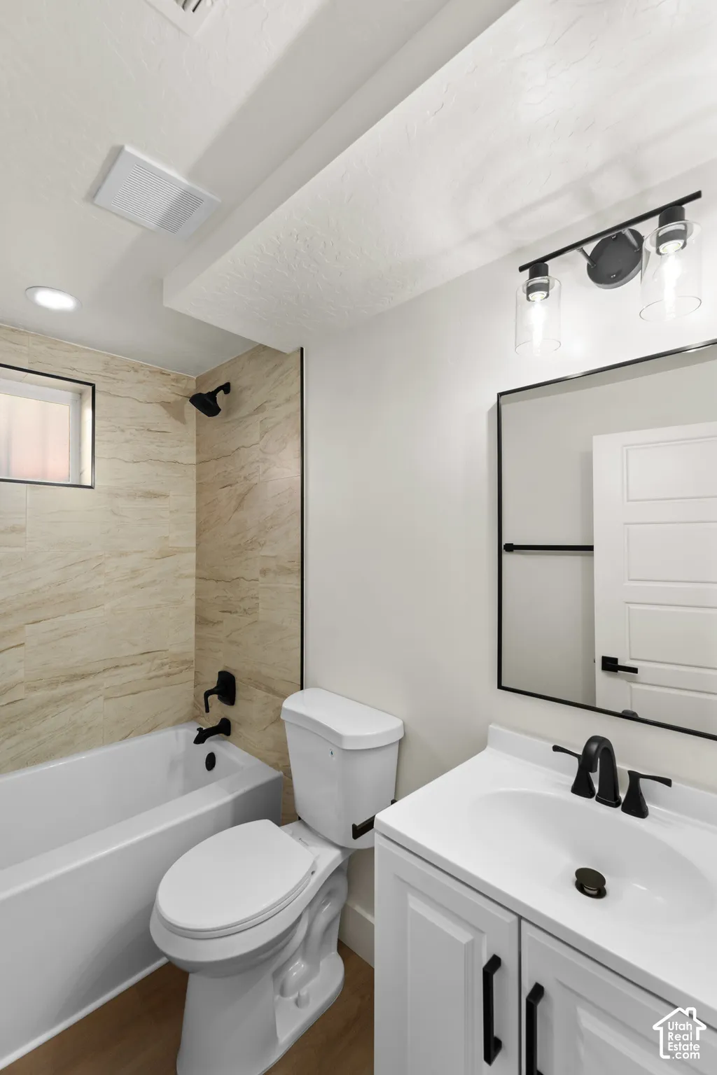 Bathroom featuring a white vanity cabinet with a contrasting countertop, matte black fixtures, a framed vanity mirror, and tub-shower surround with neutral-toned tile