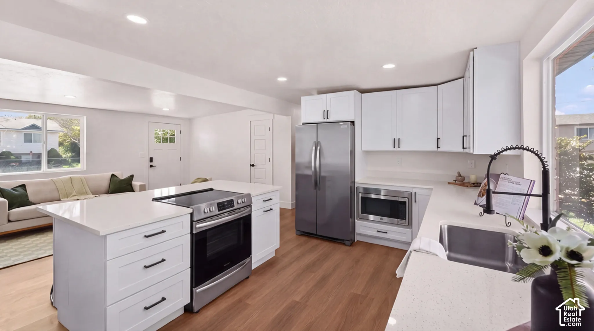 Kitchen featuring white cabinetry, wood-finish flooring, quartz countertops, a central island with a built-in range, and stainless steel appliances