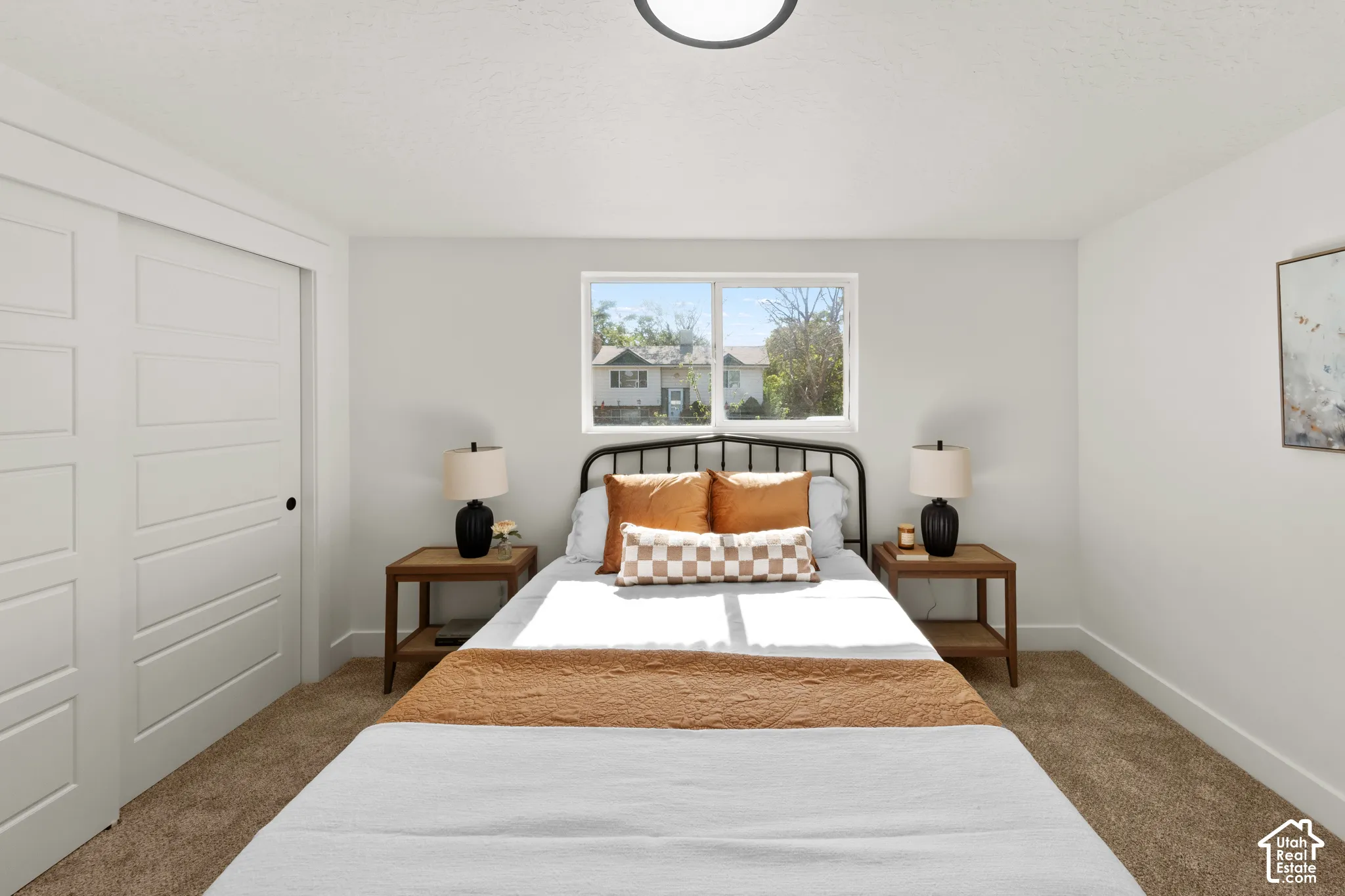Neutral-toned interior space featuring sliding multi-panel closet doors, wall-to-wall carpeting, a centered horizontal window, and a modern flush-mount ceiling light fixture