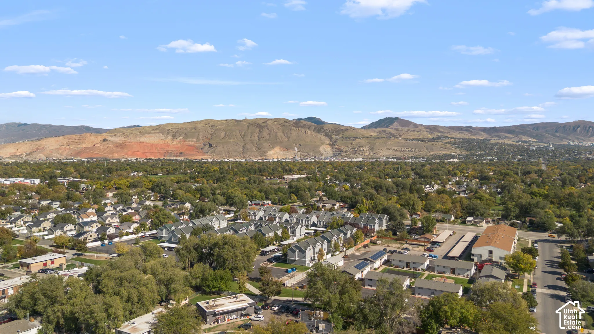 Aerial perspective of suburban landscape featuring expansive mountain ranges, mature trees, and established street grids