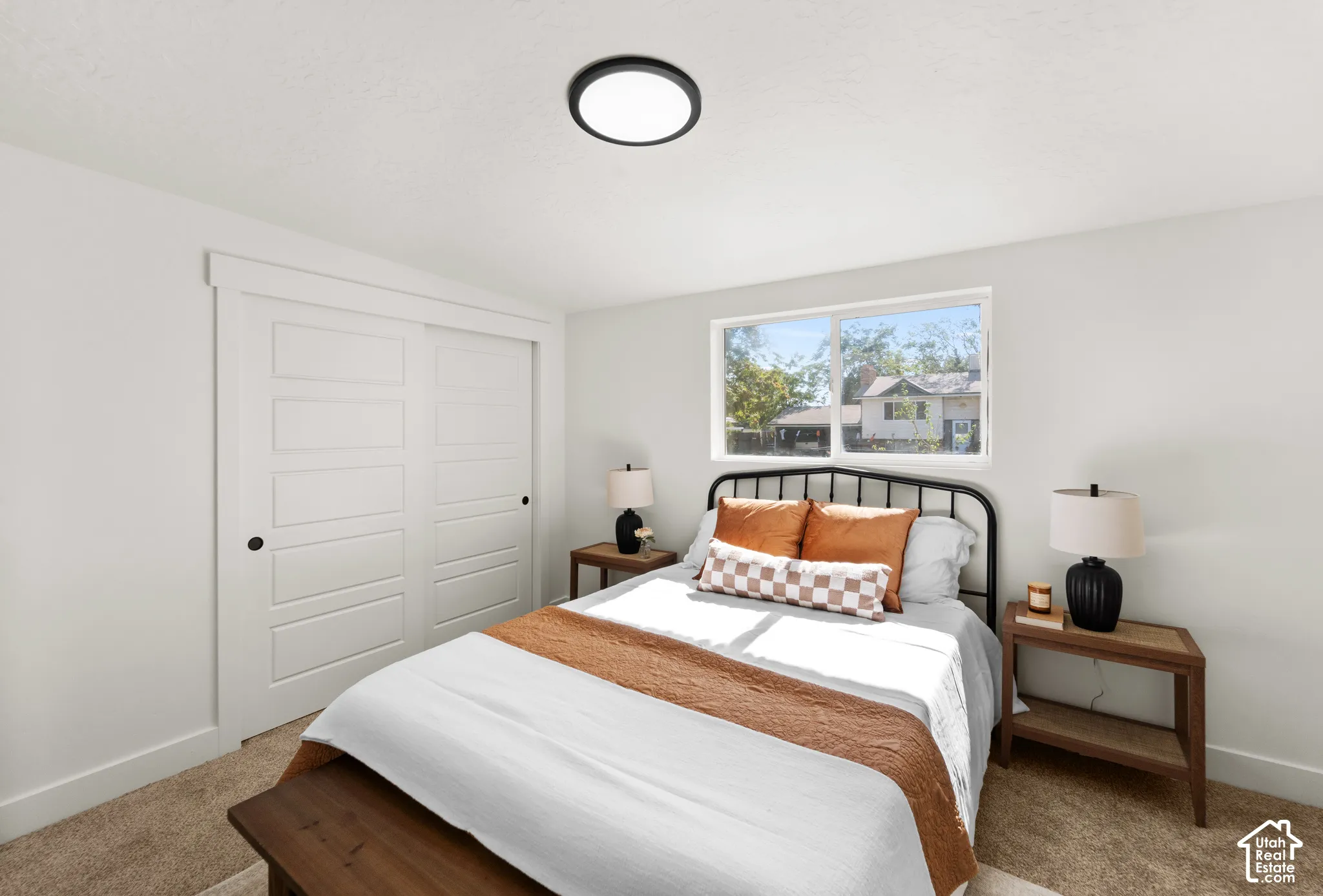 Neutral-toned room featuring wall-to-wall carpeting, a horizontal sliding window, and a white sliding closet door with a shaker-style panel design, completed by a matte black circular flush-mount ceiling light fixture