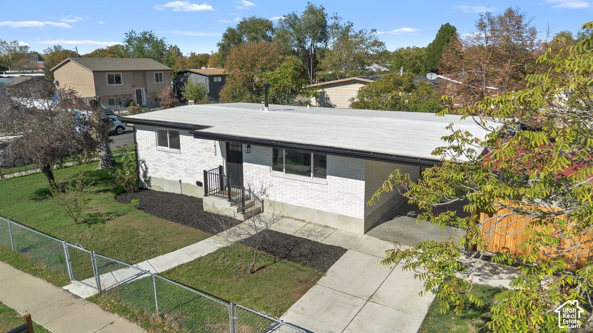 Exterior featuring white brick siding, a flat roofline, an attached carport, a concrete driveway, and black metal handrails