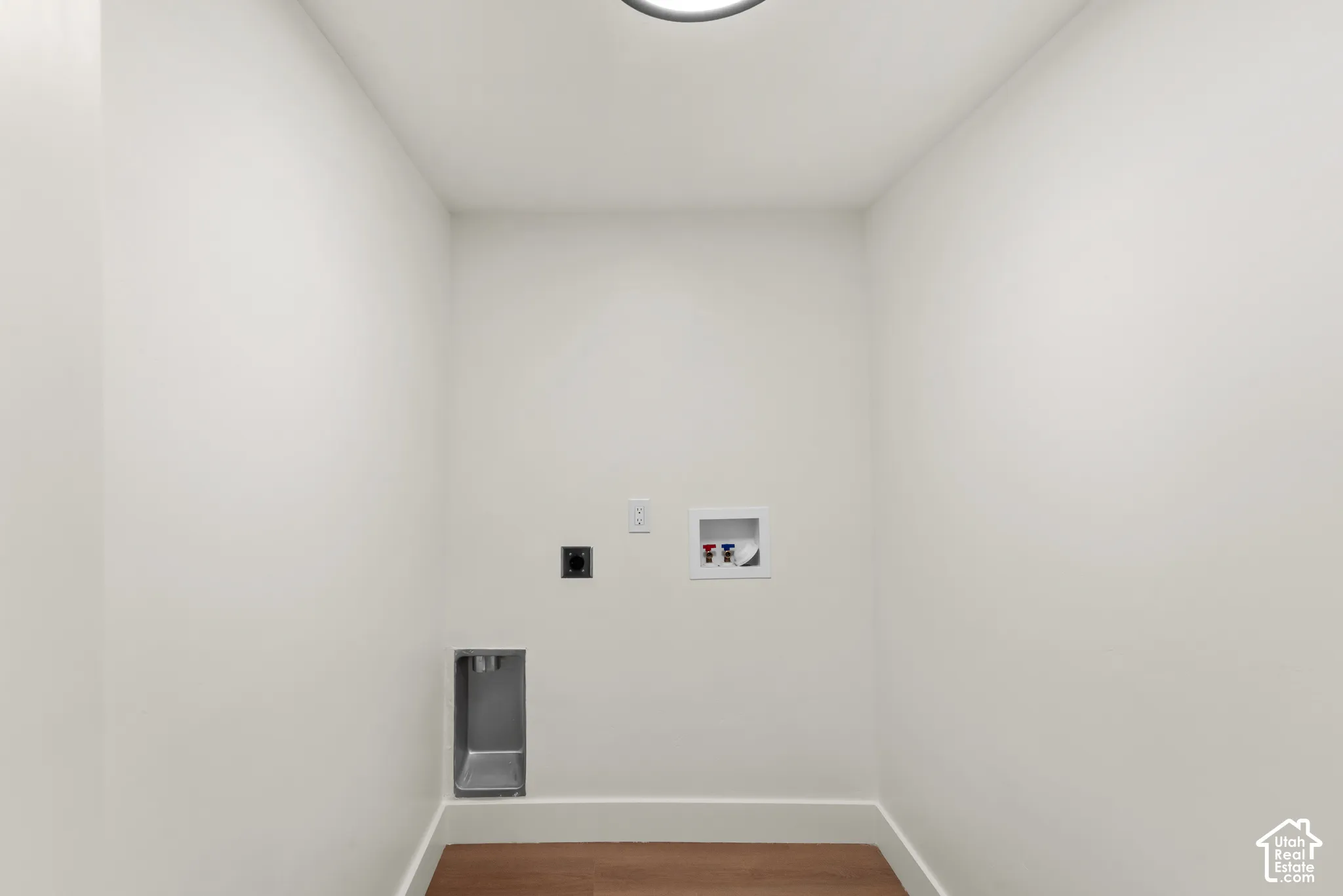 Laundry utility area featuring wood-finish flooring, recessed dryer vent, electrical outlet, and plumbing connections for a washer