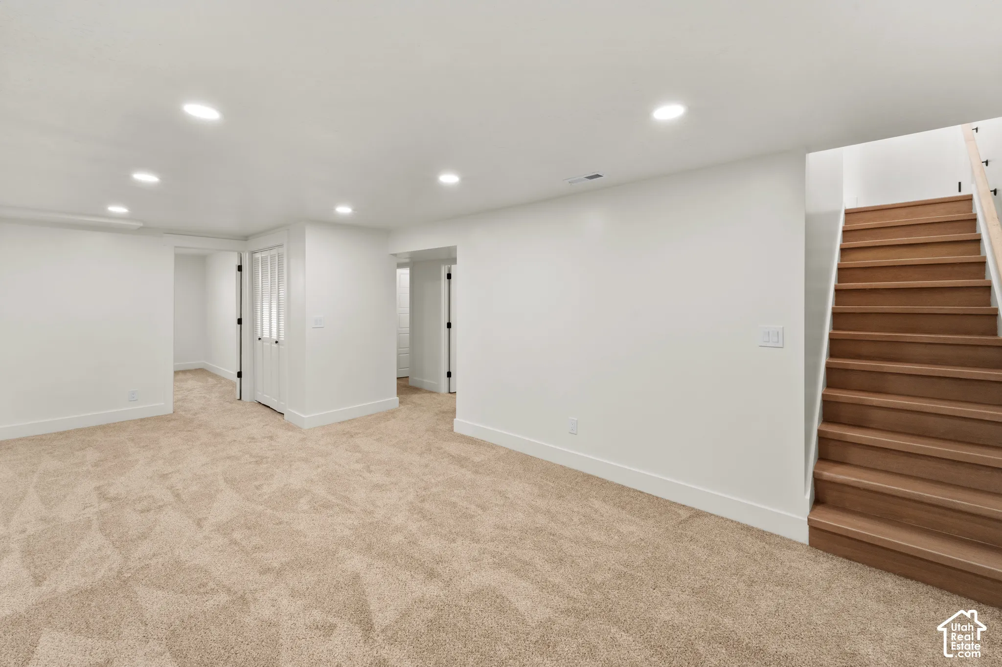 Open-concept interior featuring neutral carpeting, recessed ceiling lighting, and a staircase with wood-finish treads