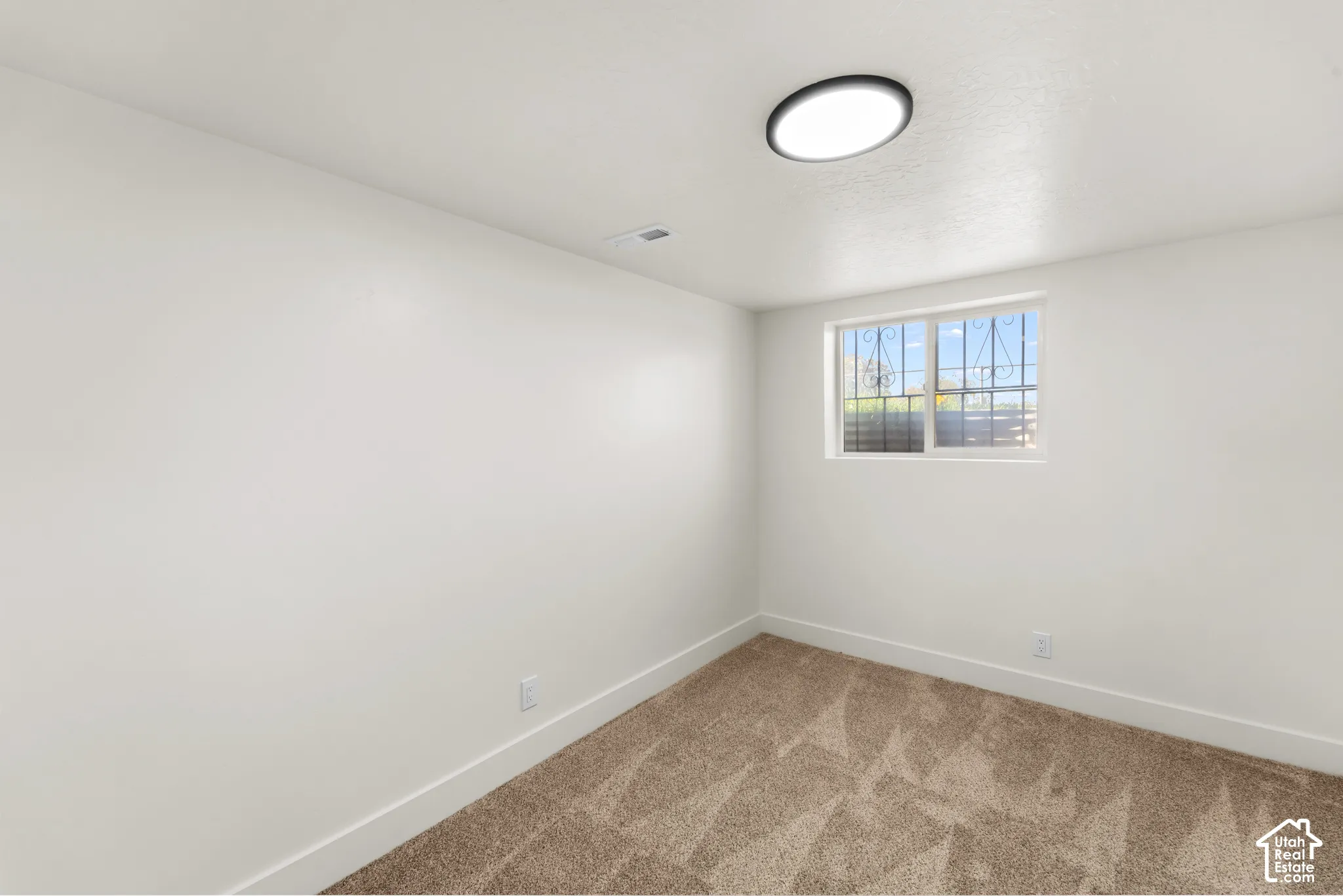 Neutral-toned carpeting, smooth-finish walls, ceiling-mounted light fixture, and horizontal slider window with metal security grilles