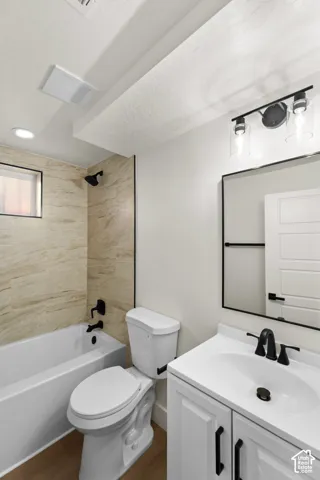 Bathroom featuring a white vanity cabinet with a contrasting countertop, matte black fixtures, a framed vanity mirror, and tub-shower surround with neutral-toned tile