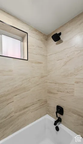 Full-height beige tile surround with natural veining, matte black showerhead, matching matte black plumbing fixtures, and a recessed window with a black frame