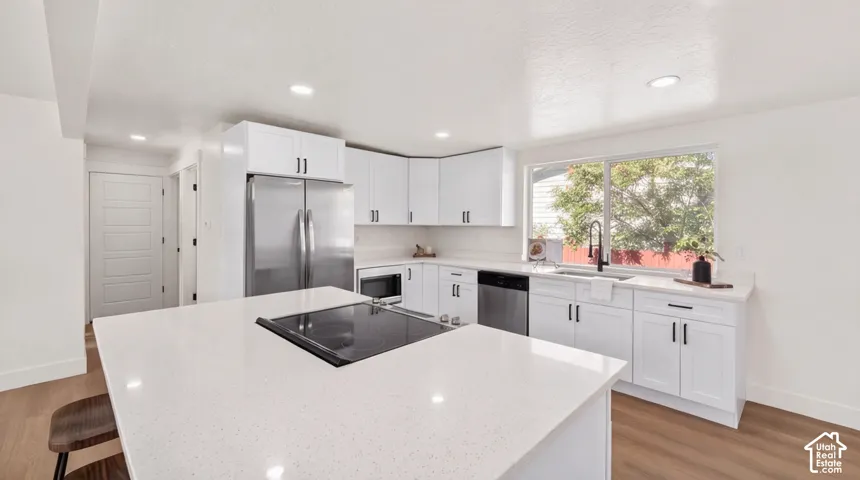 Kitchen featuring white shaker cabinetry, stone-finish countertops, stainless steel appliances, a center island with a built-in cooktop, and wood-finish flooring