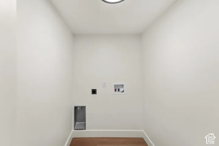 Laundry utility area featuring wood-finish flooring, recessed dryer vent, electrical outlet, and plumbing connections for a washer