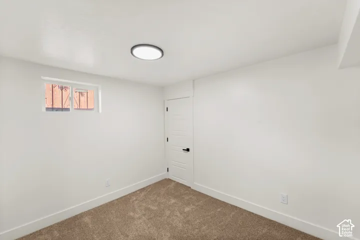 Neutral-toned wall-to-wall carpeting, recessed ceiling lighting, single-panel interior door with matte black hardware, and an egress-style window with security bars