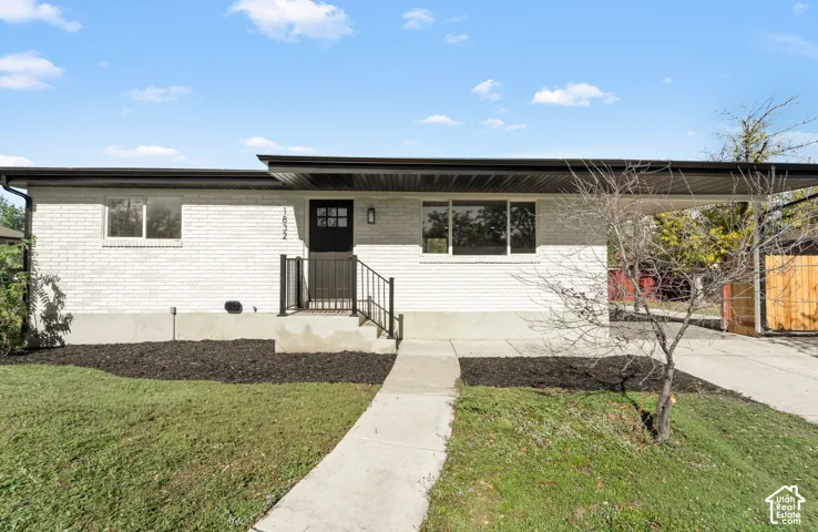 Single-story residence featuring a painted brick exterior, flat roofline, attached carport, concrete walkway, and black metal handrailing
