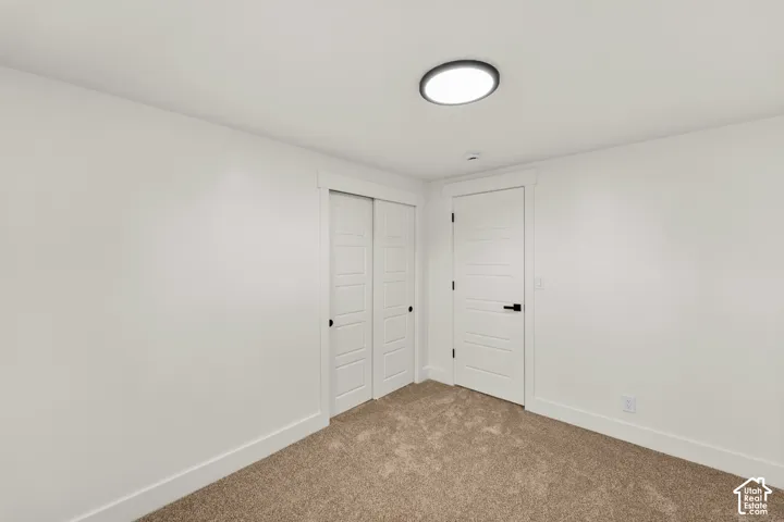 Neutral-toned carpeting, white shaker-style interior door, sliding closet doors with matching trim, and a flush-mount circular LED light fixture