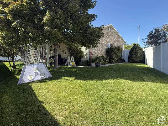 Backyard featuring a manicured lawn, mature trees, masonry exterior, and vinyl perimeter fencing