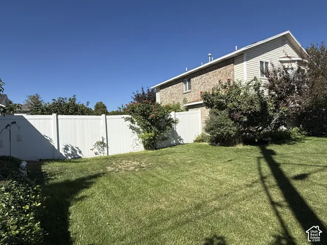 Backyard featuring a grass lawn, white vinyl fencing, and established trees