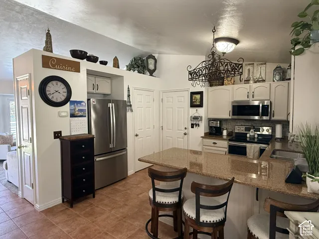 Kitchen featuring stone countertops, stainless steel appliances, white cabinetry, decorative wrought-iron chandelier, and tile flooring