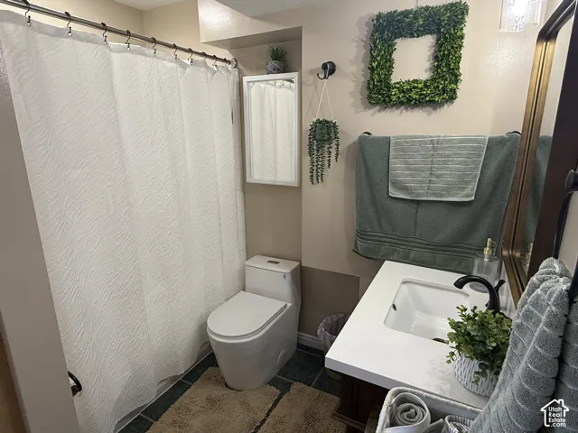 Bathroom featuring a vanity with a white rectangular sink and countertop, matte black faucet, wall-mounted medicine cabinet, and dark stone-finish tile flooring