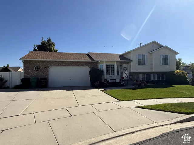 Split-level exterior featuring light siding, brick veneer accents, a multi-pane bay window, an attached two-car garage, and a concrete driveway