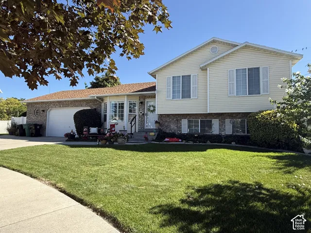 Split-level exterior featuring brick and light-colored siding, a wide concrete driveway, an attached garage, and a manicured front lawn