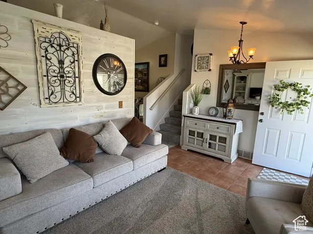 Interior space featuring a white-washed wood plank accent wall, ceramic tile flooring, neutral carpeting, a staircase with carpeted treads, and a multi-arm hanging light fixture