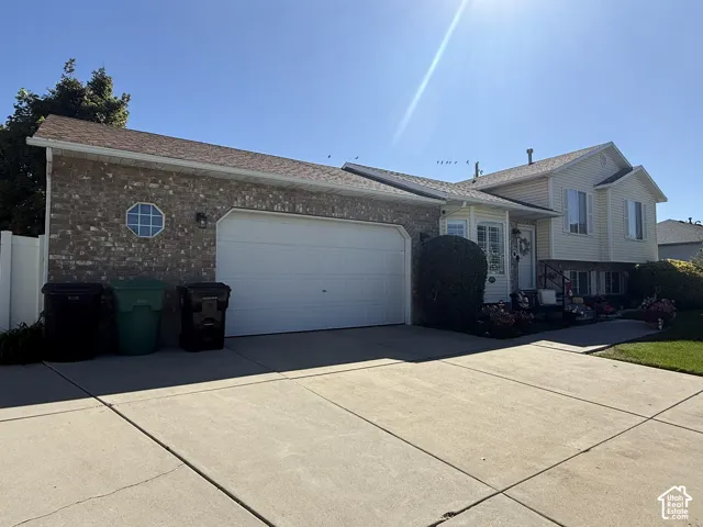 Split-level exterior featuring a brick facade, vinyl siding, a two-car garage, an octagonal accent window, and a concrete driveway