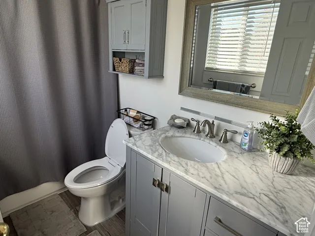 Bathroom vanity featuring a stone countertop with an integrated basin, gray shaker-style cabinetry, a coordinating wall-mounted storage cabinet, and a framed mirror