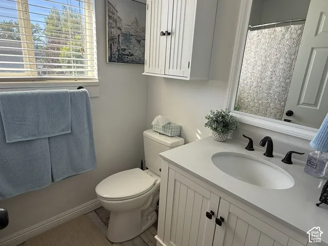 Bathroom featuring a white beadboard vanity, quartz-style countertop, undermount sink with matte black hardware, wall-mounted storage cabinet, and window with built-in blinds