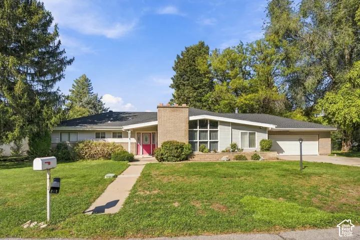 Single-story residence featuring a brick chimney, multi-pane floor-to-ceiling windows, attached garage, and mature landscape
