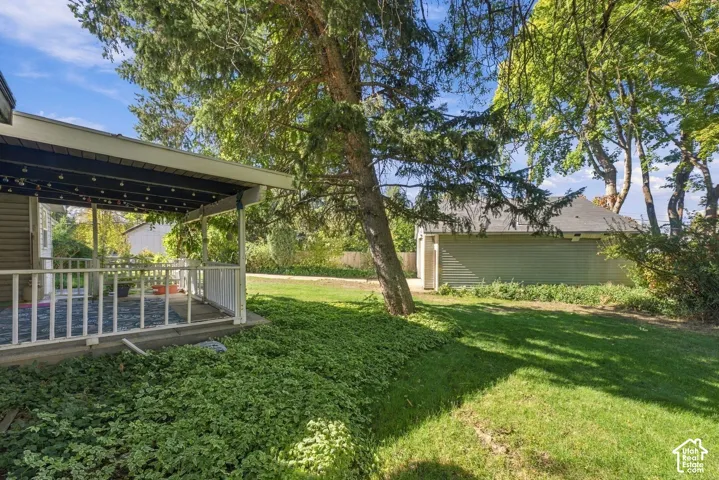 Covered porch with white railings, expansive lawn, detached garage, and mature trees