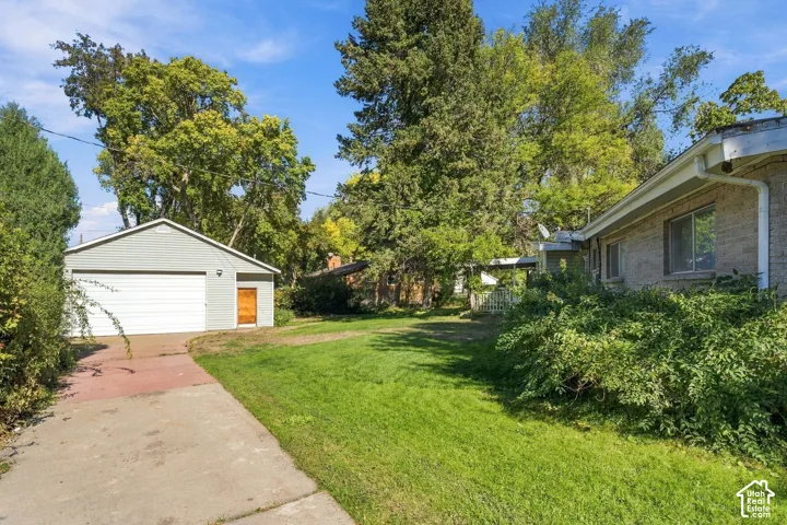 Detached garage featuring horizontal siding, expansive lawn, mature tree canopy, concrete driveway, and masonry exterior wall