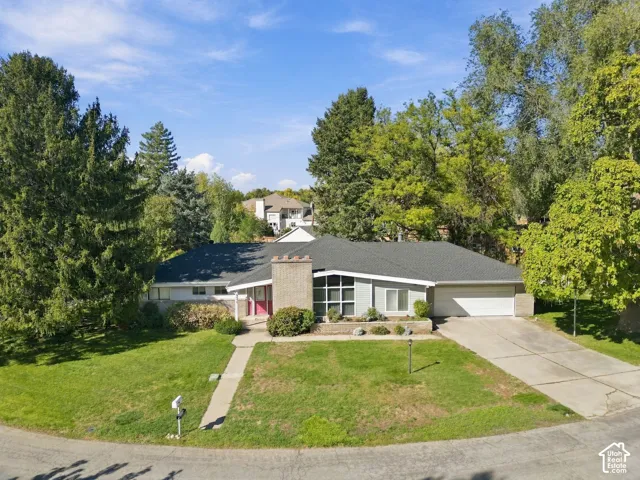 Single-story residence featuring a brick chimney, multi-pane floor-to-ceiling windows, an attached two-car garage, and mature tree landscaping
