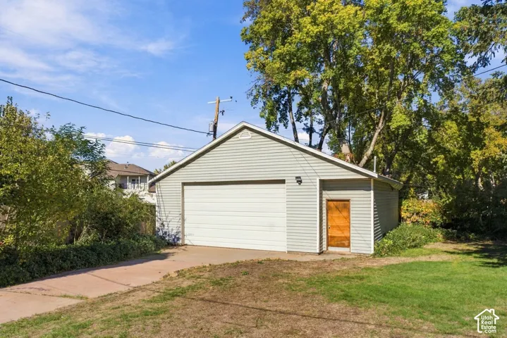 Detached garage with light-colored horizontal siding, a wide metal roll-up door, a solid wood-finish entry door, and a concrete driveway