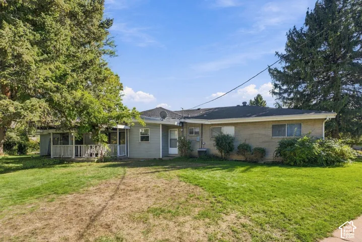 Single-story residence featuring a brick and horizontal siding exterior, expansive lawn, covered patio, and mature trees