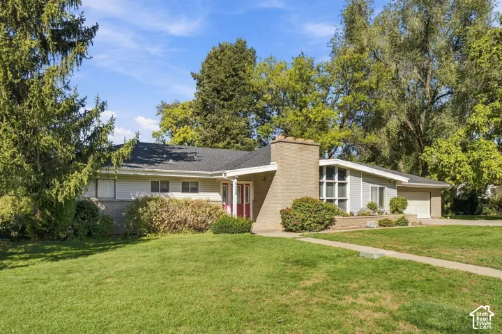 Ranch-style exterior featuring horizontal siding, a prominent brick chimney, multi-pane floor-to-ceiling windows, and an attached garage
