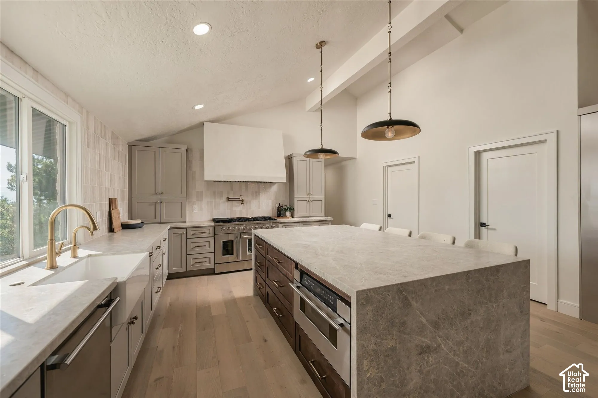 Kitchen featuring a central island with stone-finish countertops, apron-front sink with brass-finish faucet, custom cabinetry, stainless steel range with a custom hood, and wood-finish flooring