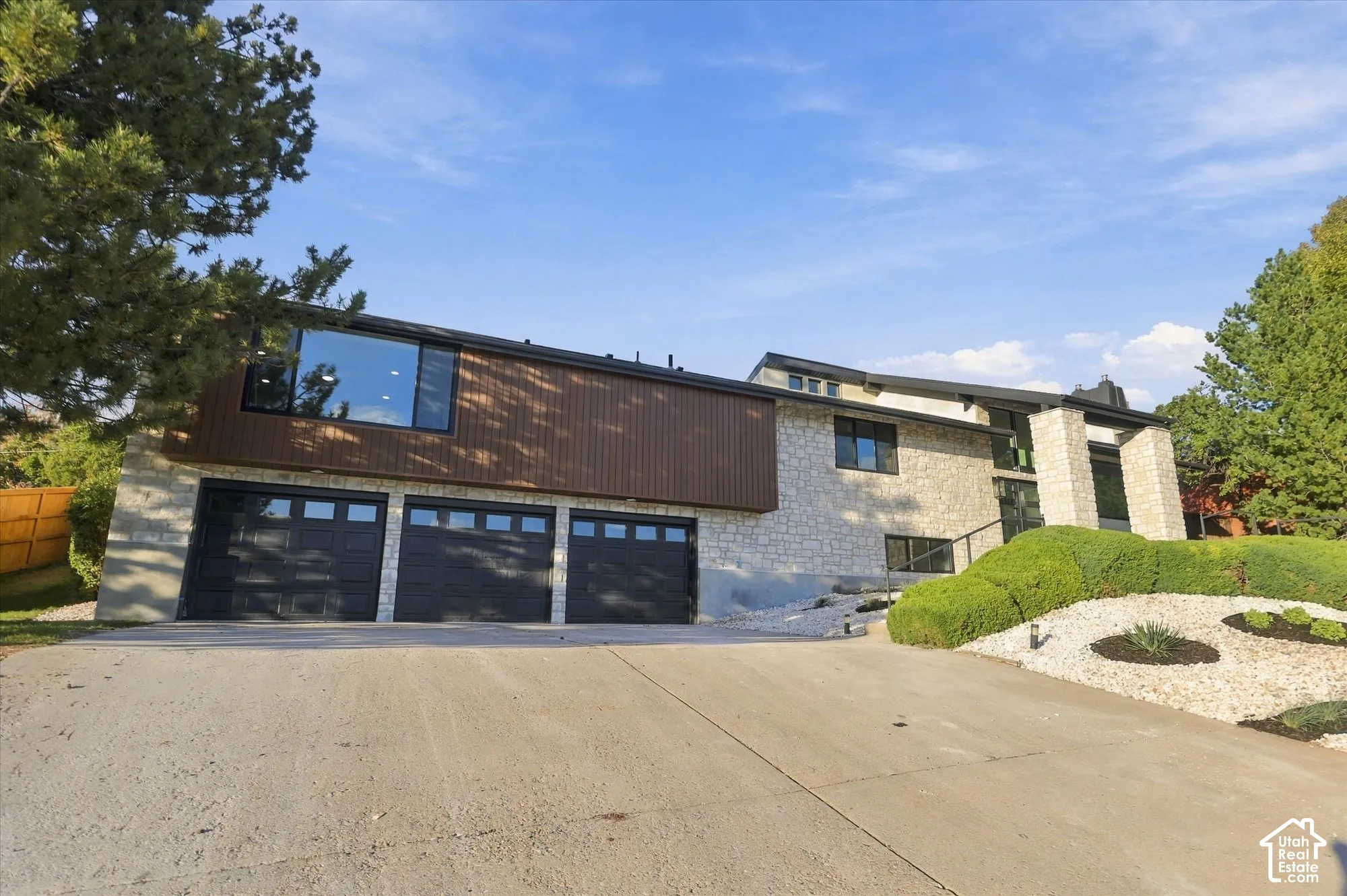 Multi-level exterior featuring stone masonry, vertical wood-finish siding, a three-car garage with glass-panel doors, and xeriscaped landscaping