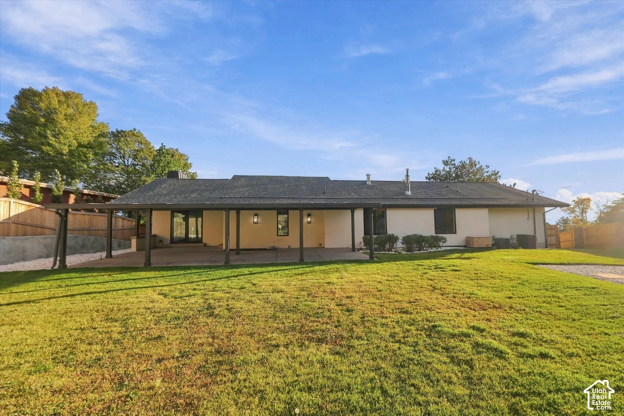 Rear exterior featuring an expansive covered patio, a concrete foundation, a sprawling lawn, and wood privacy fencing
