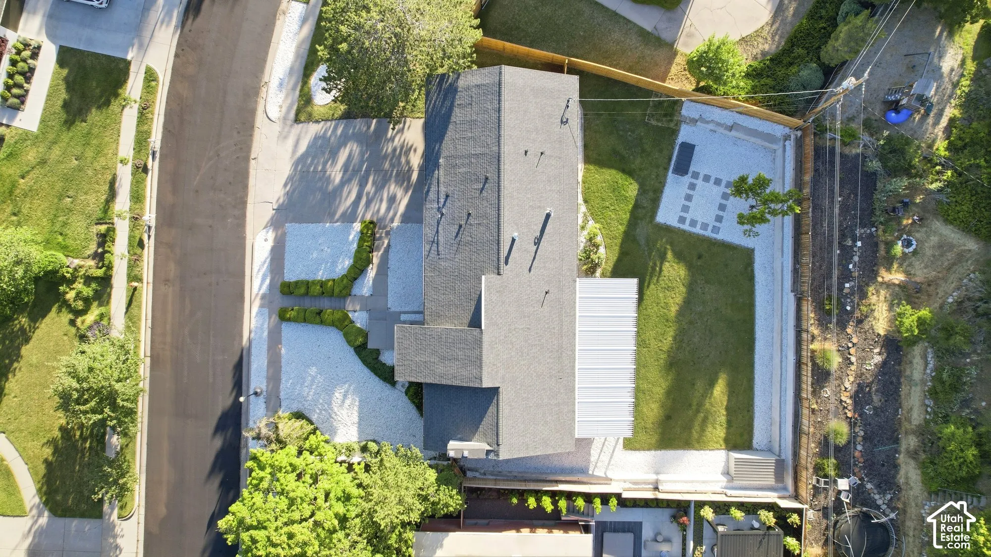 Aerial perspective of a property featuring a multi-level concrete patio, a structured lawn area, a paved driveway, and mature landscaping