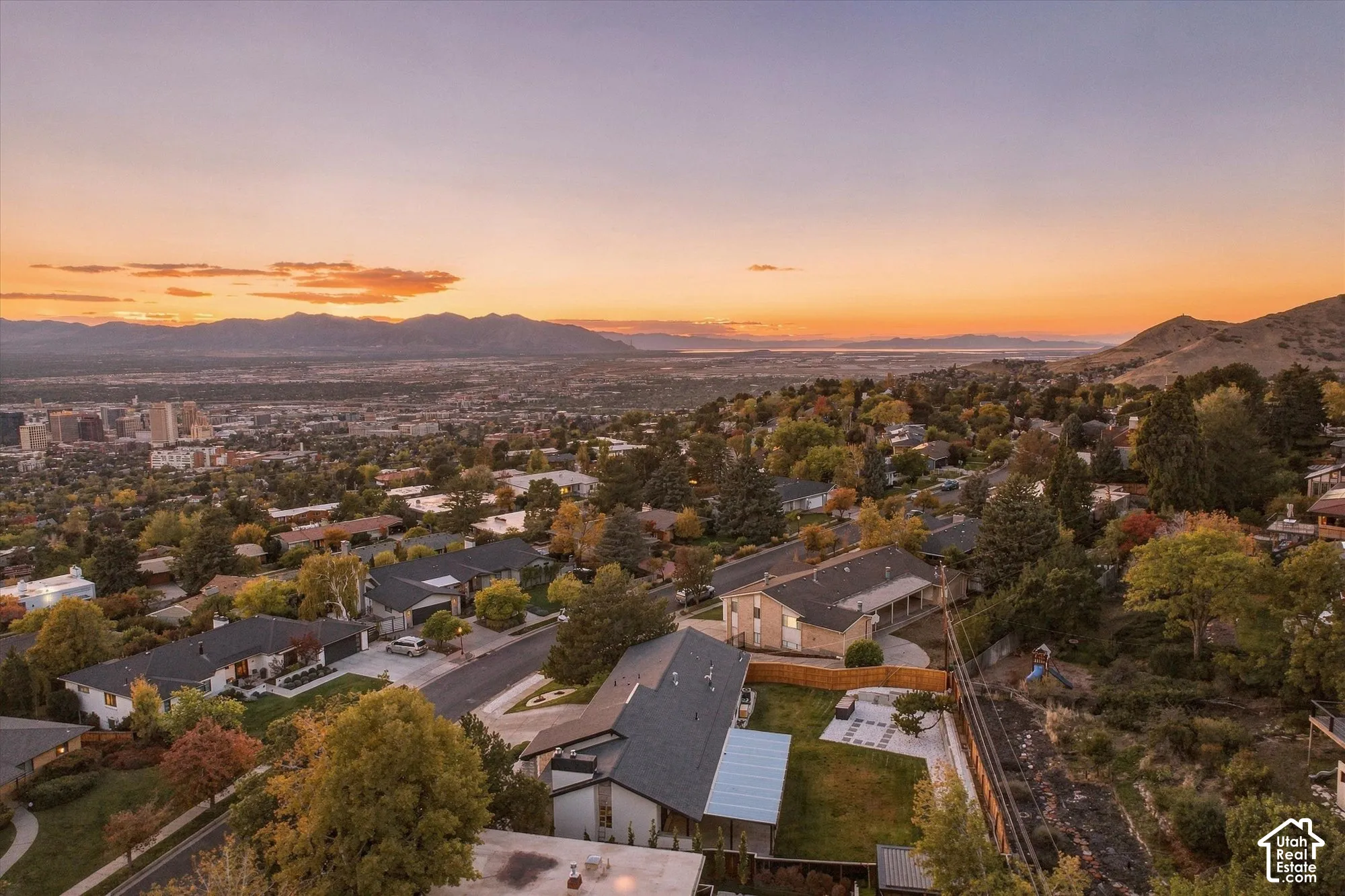 Elevated hillside property featuring a paved rear patio, mature trees, multi-level rooflines, and a mountain and valley backdrop