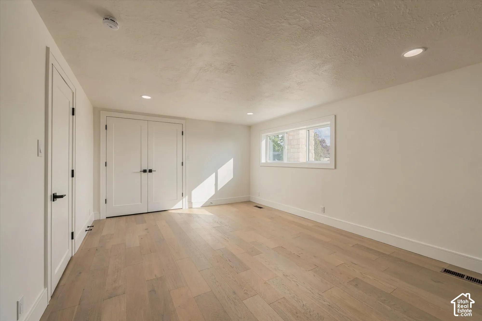 Neutral-toned room featuring wide-plank wood-finish flooring, double doors with matte black hardware, recessed lighting, and a single-pane window