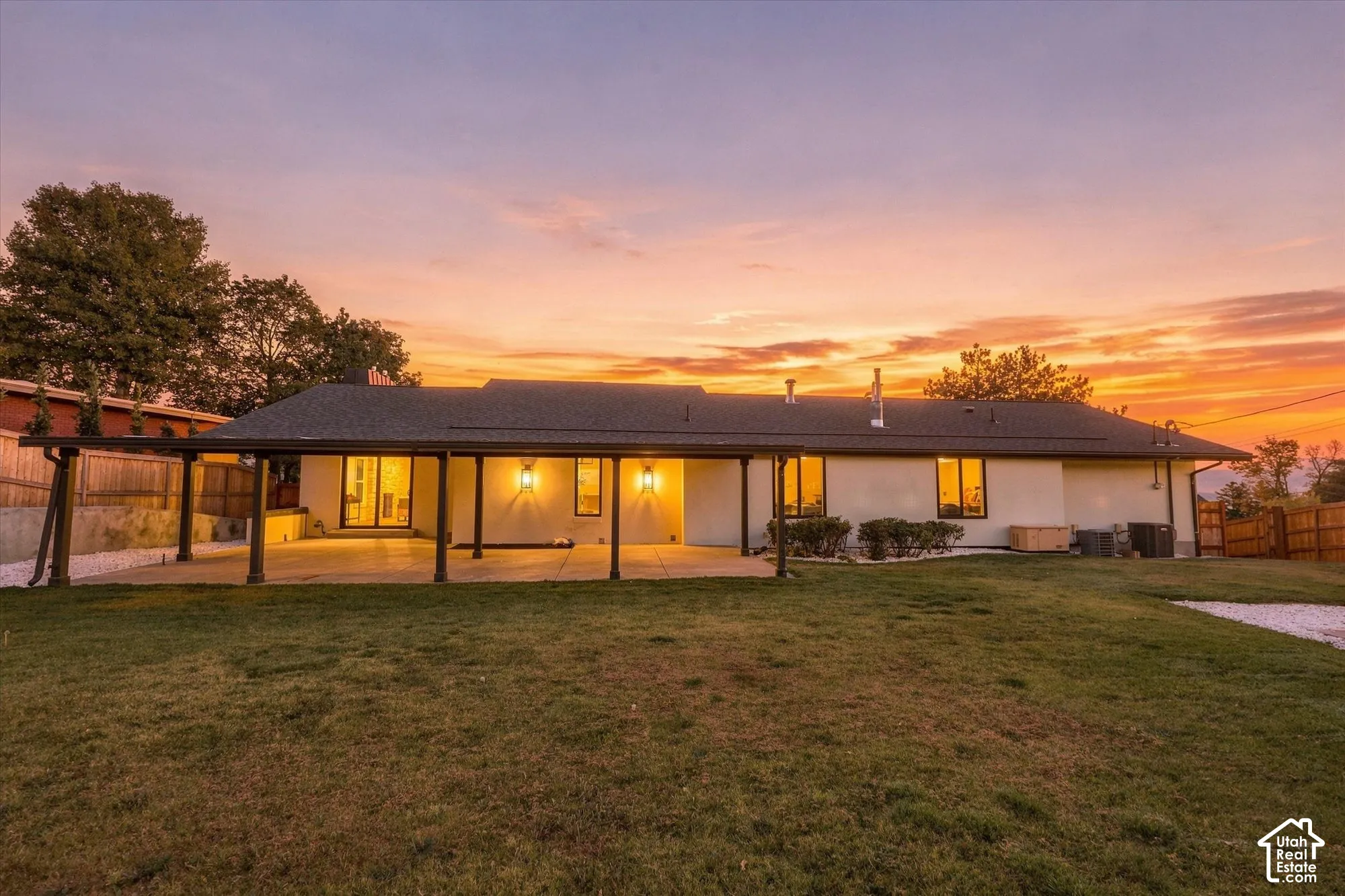 Covered concrete patio with post-and-beam support, stucco exterior, expansive lawn, and fenced perimeter